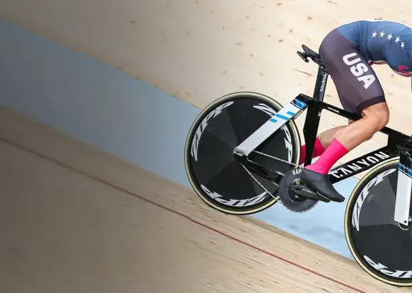 A determined track cyclist in a USA kit races on a wooden velodrome, pushing hard for victory.