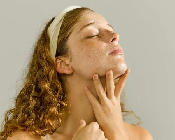 A young woman with freckles enjoys a relaxing skin care massage, her eyes closed in bliss.