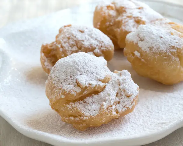 Vier goldbraune rheinische Krapfen, bestäubt mit Puderzucker, liegen auf einem weißen Teller.