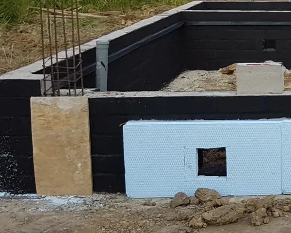 Fundament z czarną izolacją przeciwwilgociową i płytami XPS. Widać zbrojenie i fragmenty szalunku. Dobra jaka izolacja na fundament.
