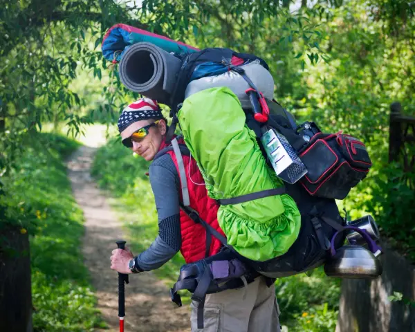 Un randonneur, prêt pour l'aventure, montre comment porter un sac à dos bien chargé avec une couverture de sol et une bouilloire.