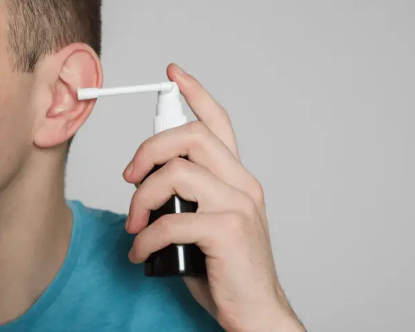 Mężczyzna aplikuje spray do ucha, łagodząc płyn w komórkach wyrostka sutkowatego.
