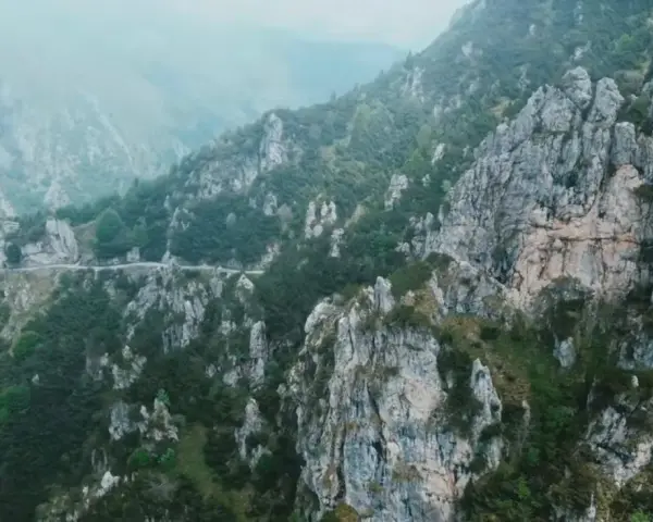 Strada tortuosa che sale verso il passo Barmone, tra rocce imponenti e vegetazione lussureggiante.