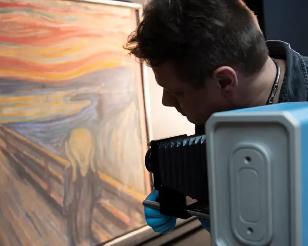 En man med blå handskar fotograferar "Skriet". Vem har målat skriet? Edvard Munch.