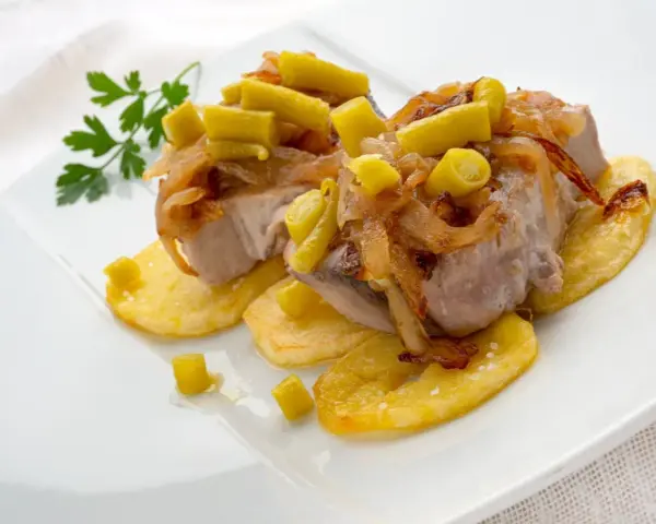 Bonito al horno sobre patatas, con cebolla caramelizada y pimientos verdes. Un plato delicioso y bien presentado.