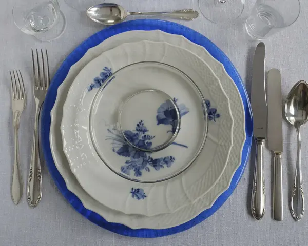 Vacker dukning med blå och vit porslin, bestick och glas. En elegant dessert tallrik väntar på att fyllas.