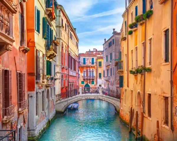 Canale veneziano con palazzi colorati e un ponte. Si immagina come fu costruita Venezia, su palafitte e ingegno.