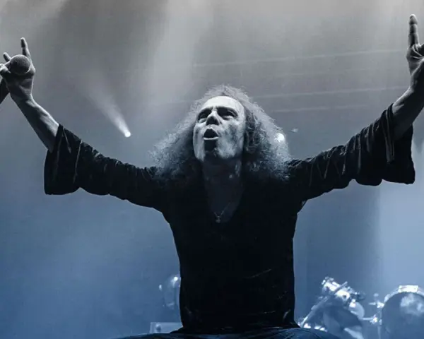 Ronnie Dio mit erhobenen Armen und Mikrofon, die Hand zum "Rock on"-Gruß geformt.