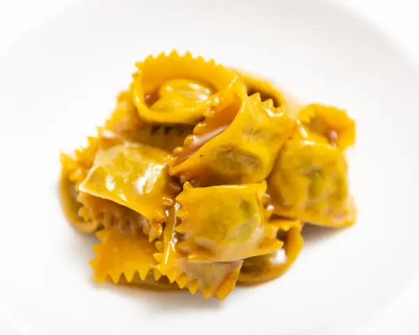 Un mucchietto di ravioli del plin, dorati e conditi con un sugo cremoso, su un piatto bianco.