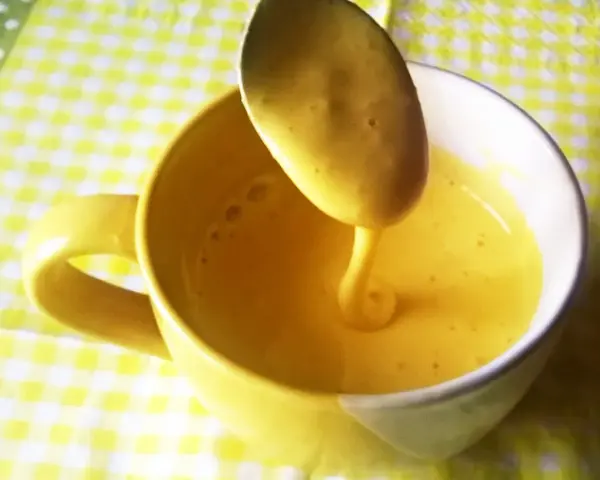 Kogel mogel przepis w filiżance, łyżka z gęstym, żółtym kremem spływa do naczynia.