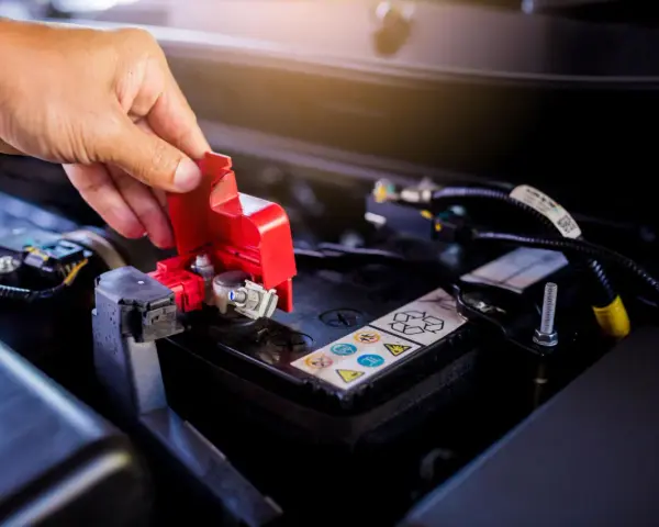 Mano che solleva il coperchio rosso di protezione del polo della batteria, un passo fondamentale per imparare come cambiare la batteria della macchina.