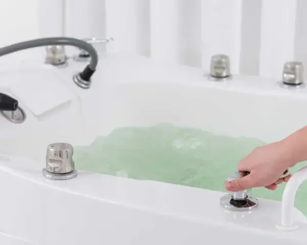 Dłoń reguluje strumień wody w wannie, przygotowując relaksujący masaż wirowy.