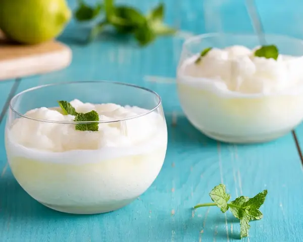 Due bicchieri di sorbetto al limone senza albume, guarniti con menta fresca, su un tavolo di legno blu.