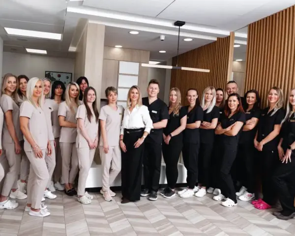 Grupa uśmiechniętych dentystów i personelu medycznego w jasnych i ciemnych uniformach stoi w nowoczesnym gabinecie.