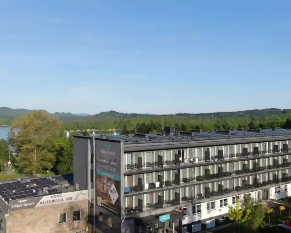 Widok na hotel Solina Resort & Spa z apartamentami i pokojami, otoczony zielenią, z jeziorem Solina w tle.