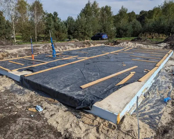 Płyta fundamentowa z folią i drewnianymi elementami na budowie domu szkieletowego.