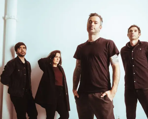 Quatre musiciens, un groupe rock canadien francophone, posent devant un mur blanc.