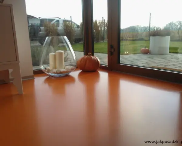 Pomarańczowa podłoga z żywicy, z widocznym blaskiem i odbiciami. Wazon ze świecami i dynia dodają jesiennego klimatu.