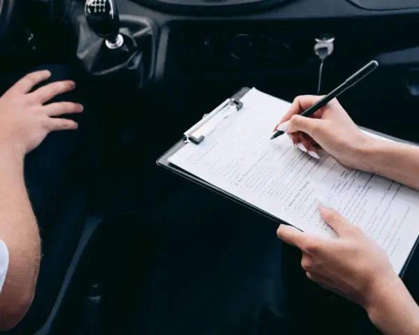 Kobieta wypełnia formularz rejestracji auta, siedząc obok kierowcy.