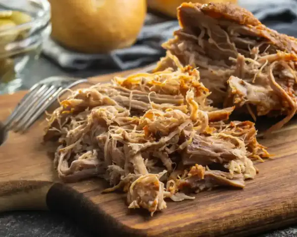 Un délicieux effiloché de porc, tendre et savoureux, prêt à être dégusté sur une planche en bois.