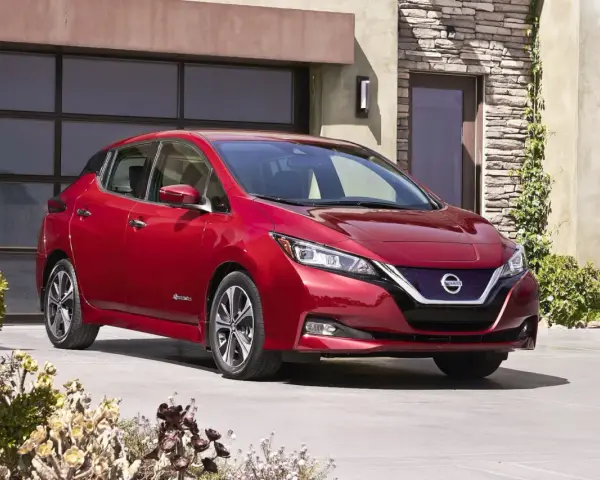 Czerwony Nissan Leaf przed nowoczesnym domem. Sprawdź atrakcyjną nissan leaf cena i wybierz swój wymarzony samochód elektryczny.