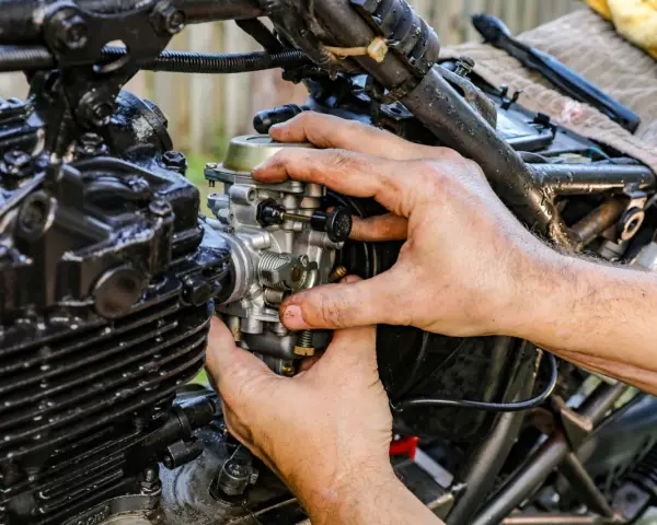 Ręce mechanika regulują gaźnik motocykla, pokazując, jak działa ssanie.