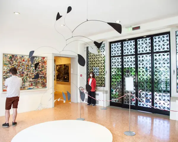 Un uomo ammira un quadro astratto, mentre una donna osserva una scultura mobile. Un'atmosfera d'arte al Peggy Guggenheim di Venezia.