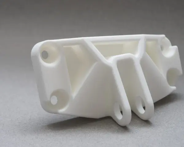 A white, complex SLS part with multiple holes and support structures, ready for assembly.