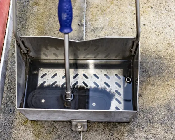En borste med blått handtag vilar i en vattenfylld smutsavskiljare av metall.