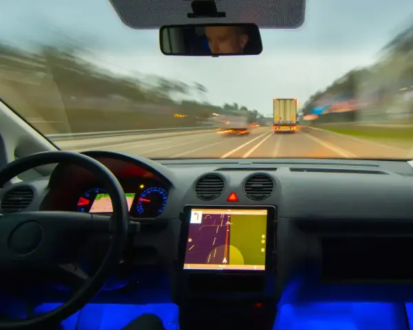 Widok z kabiny samochodu jadącego autostradą. Na desce rozdzielczej tablet z nawigacją, a obok niego system rozpoznawania znaków drogowych.