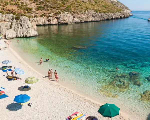 Sycylia pogoda idealna na plażowanie. Słoneczny dzień, turkusowa woda i kamienista plaża z kilkoma osobami relaksującymi się pod parasolami.