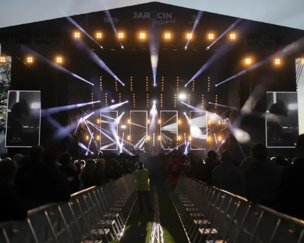 Jarocin Festiwal rozświetlony tysiącami świateł. Tłum czeka na koncert, a na scenie widać artystów.