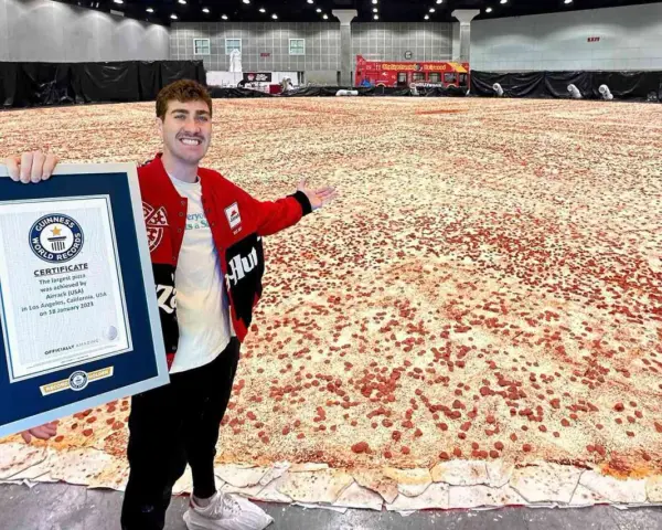 Mężczyzna prezentuje certyfikat Guinnessa za największą pizzę świata, która rozciąga się na ogromnej przestrzeni.