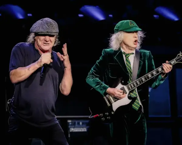 Brian Johnson i Angus Young, legendarny skład AC/DC, na scenie. Brian śpiewa do mikrofonu, Angus gra na gitarze.
