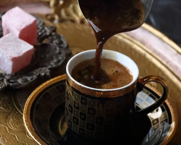 Gorąca, aromatyczna kawa, jedna z najmocniejszych kaw, nalewana do ozdobnej filiżanki. Obok słodkie lokum.