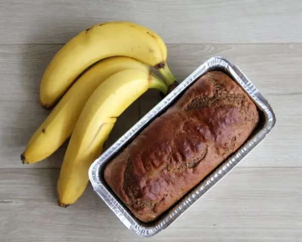 Gotowy proteinowy chlebek bananowy w formie, obok pęk dojrzałych bananów.