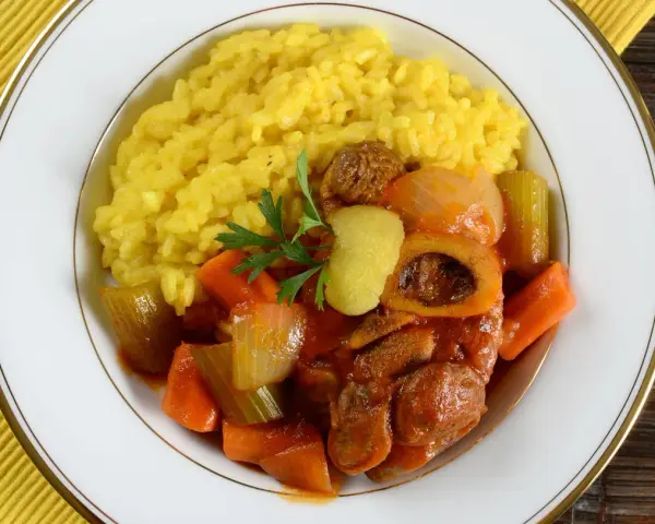 Risotto giallo e ossobuco con verdure, un classico dei piatti tipici milanesi, guarnito con prezzemolo e scorza di limone.