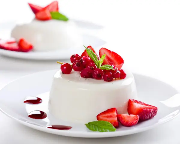 Deliciosa panna cotta cremosa adornada con fresas, grosellas rojas y menta fresca.