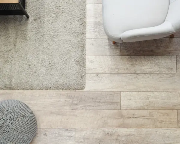 Elige el color del suelo de una casa con este suelo de madera clara, alfombra beige y puf gris.
