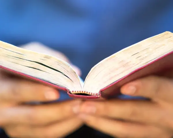 Otwarta księga z czerwonym grzbietem, trzymana w dłoniach. Może zawierać 10 przykazań bożych dla dzieci.