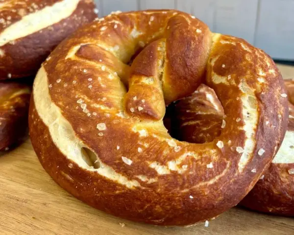 Frisch gebackene, goldbraune sauerteig brezeln mit grobem Salz bestreut, liegen auf einem Holzbrett.