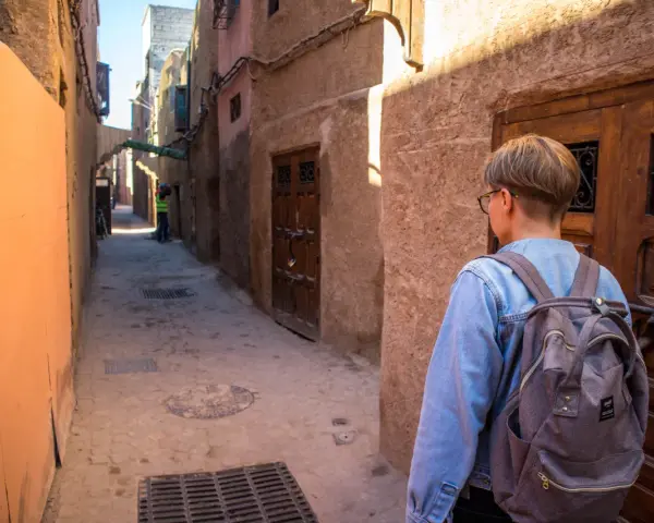 Młoda osoba z plecakiem idzie wąską uliczką w Marrakeszu. Czy w Marrakeszu jest bezpiecznie? Tak, zwiedzanie jest przyjemne.
