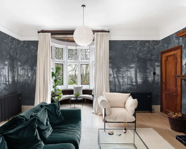 Sala con papel pintado de bosque, sofá verde, sillón beige y chimenea de madera. Ideas de como poner papel pintado para transformar tu hogar.