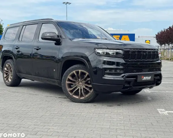 Czarny Grand Wagoneer z brązowymi felgami stoi na parkingu przed sklepami.
