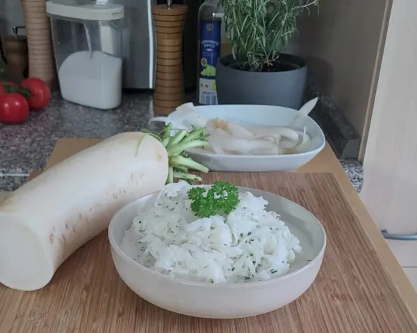 Ein frischer Rettichsalat, zubereitet nach einem einfachen Rettichsalat Rezept, garniert mit Petersilie. Daneben liegt ein ganzer Rettich.