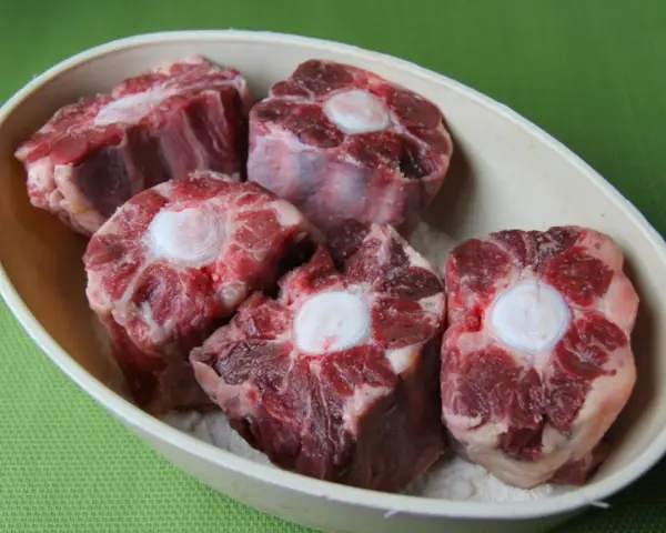 Trozo de rabo de ternera crudo en un cuenco, con el hueso central visible.
