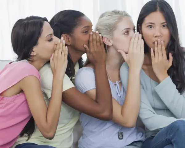 Four friends share secrets, whispering what is gossip. One girl looks surprised as the whispers continue.