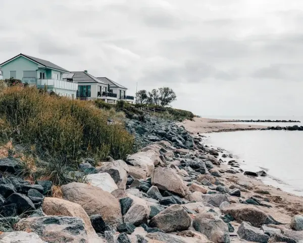 Häuser am Hang über einem steinigen Strand. Ein ruhiger Ort, der zu den Fehmarn Geheimtipps zählt.