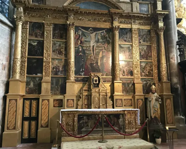The ornate altar of the Basilica of Mary Magdalene features a central crucifixion scene surrounded by smaller narrative paintings, all set within a gilded structure.