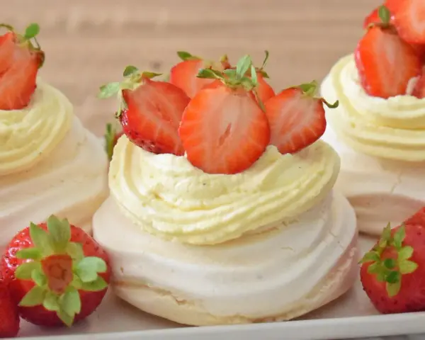 Mini torty pavlova z bitą śmietaną i świeżymi truskawkami.